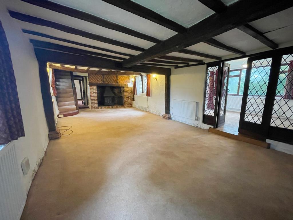 Lot: 31 - A DETACHED THATCHED COTTAGE FOR IMPROVEMENT AND REPAIR - Living room with expose beams and fireplace